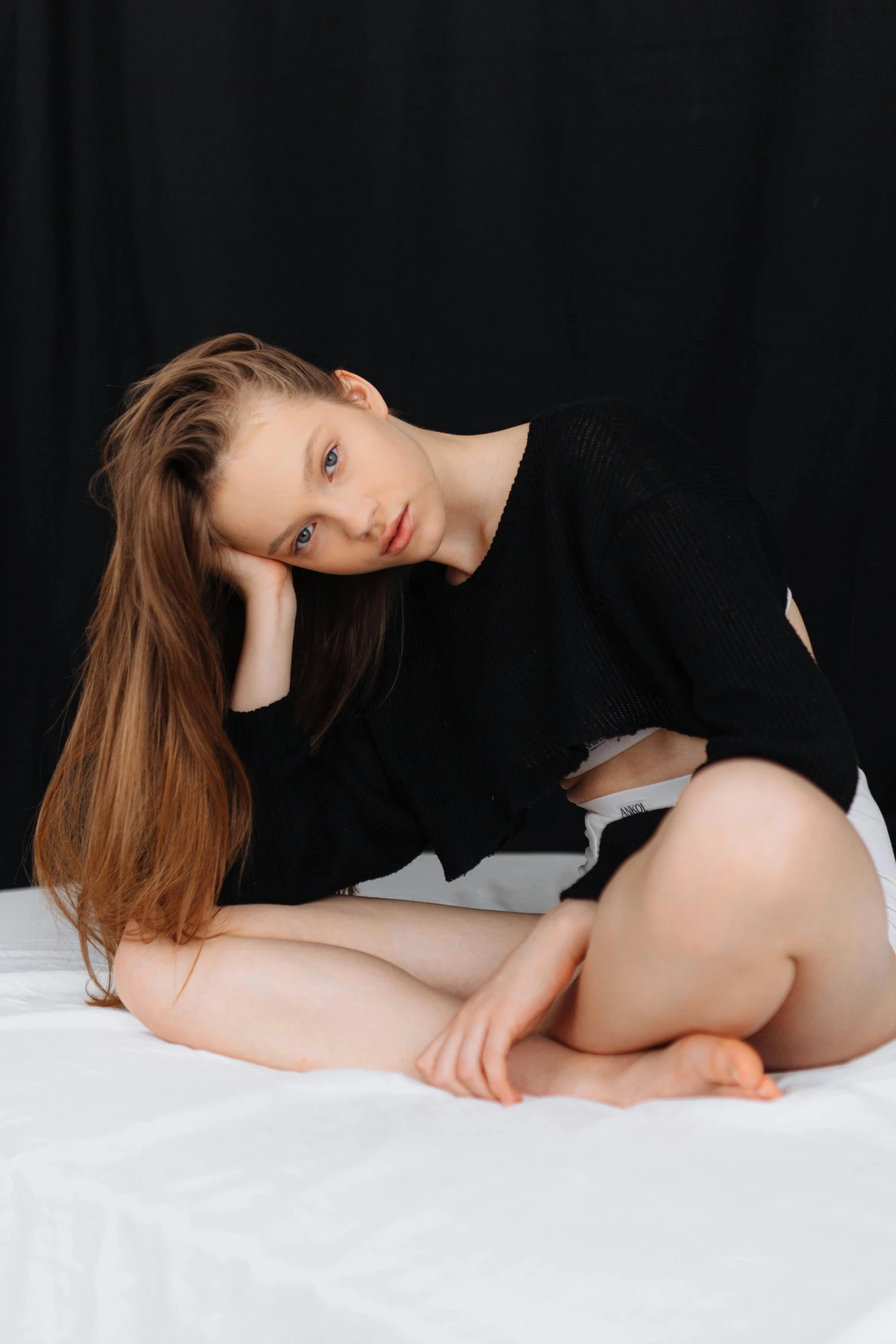 a woman sitting on a white surface next to a black backdrop