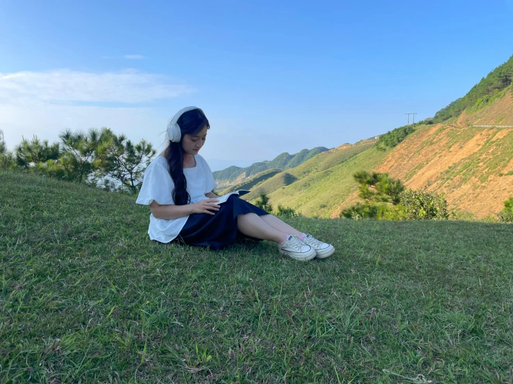 a woman sitting on top of a lush green field next to a hillside