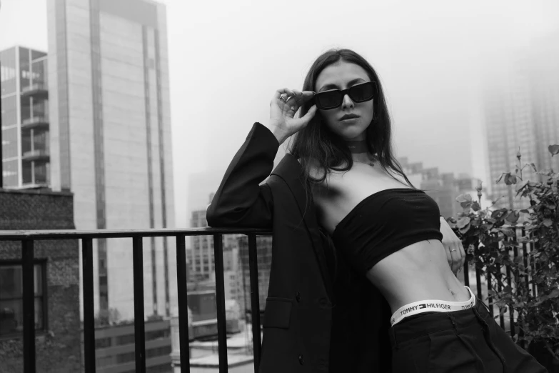 black and white po of woman wearing sunglasses leaning on fence