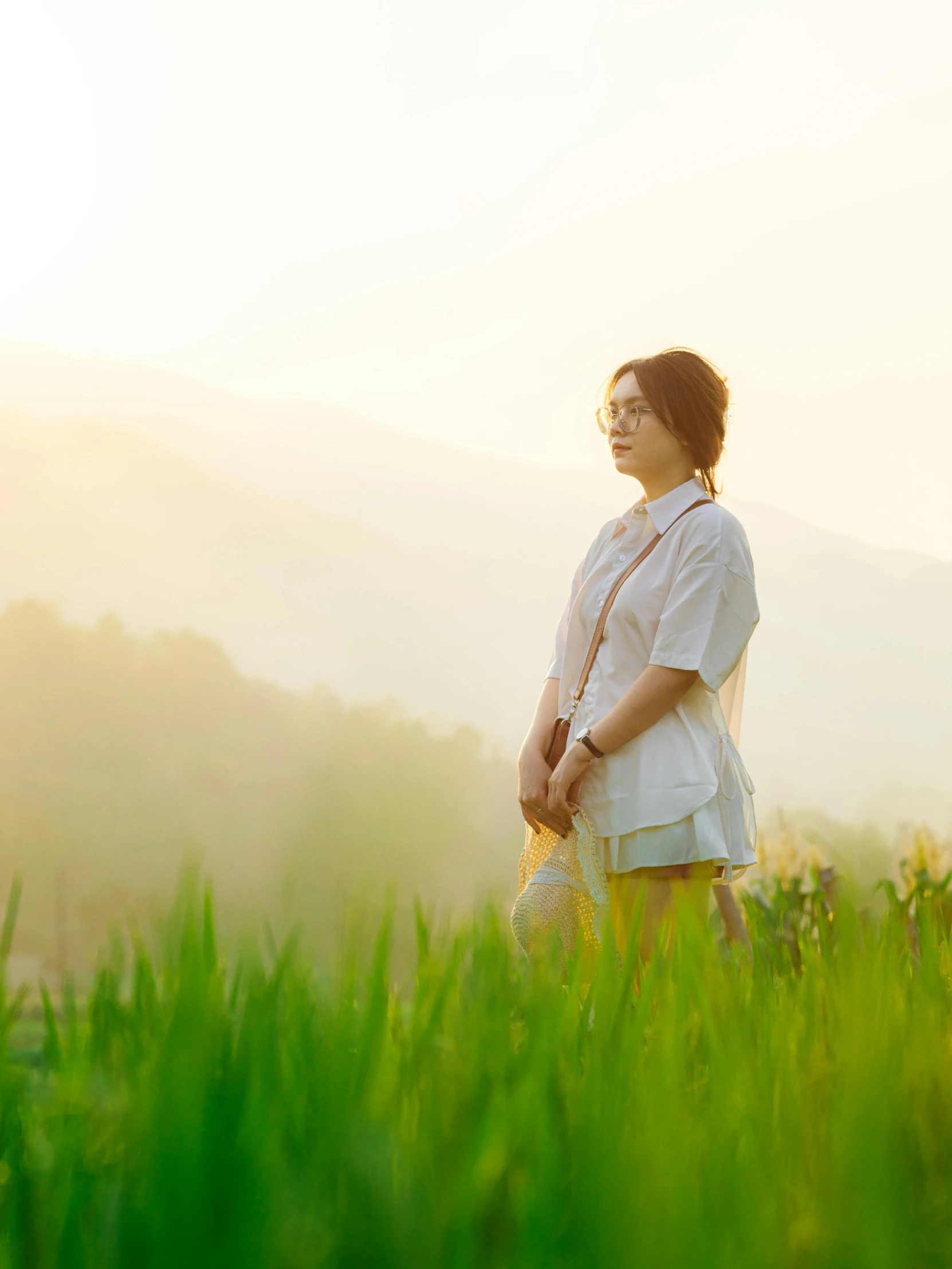 a woman stands in tall grass on a hill