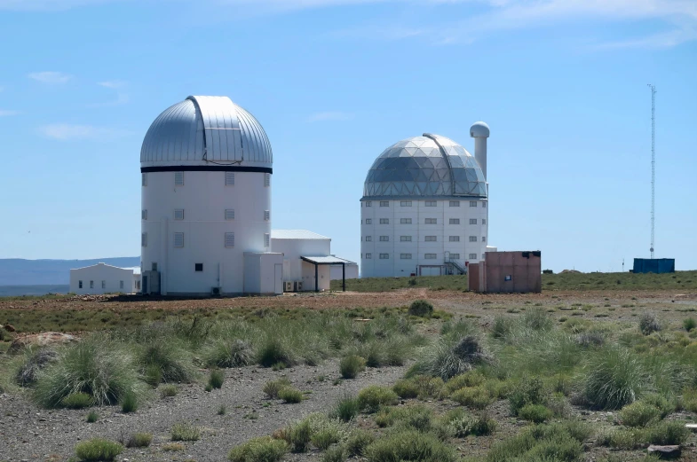 several white observatorys sit near some scrub brush