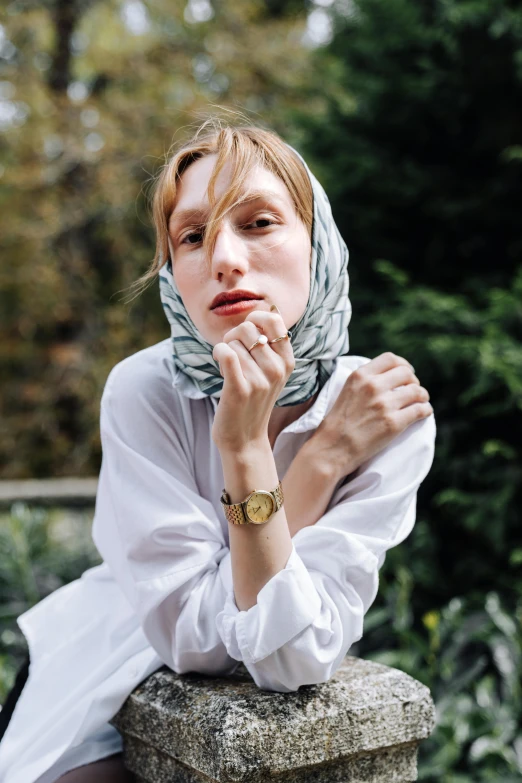 a woman sitting on a stone ledge, in white with her hands clasped to the face