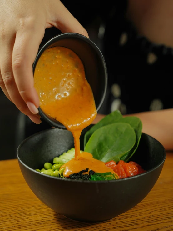 a hand is pouring sauce into a bowl with vegetables