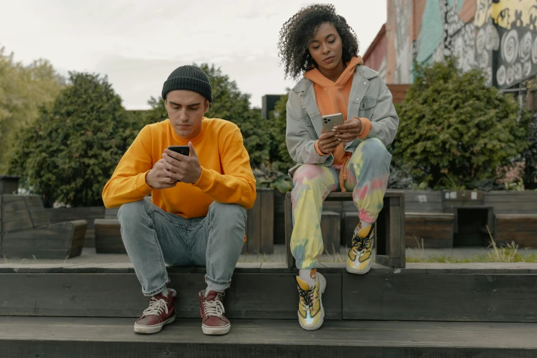 the two people sit on the step outside checking their phones