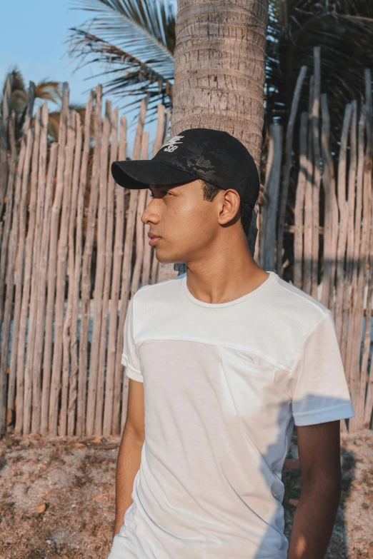 man in white t - shirt and hat sitting next to a wooden fence