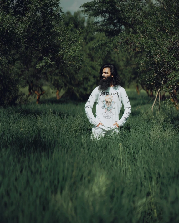 an artistic man sitting in tall grass and surrounded by trees