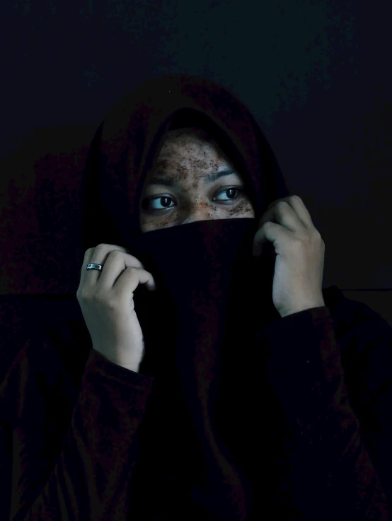 a person standing in the dark hiding her face behind a sheet