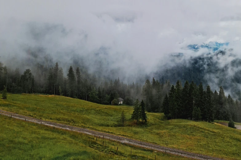 a grassy green hillside and a small house in the distance with clouds moving over them