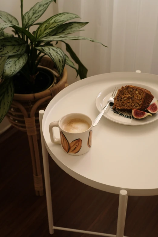 a small white table with a cup and plate with cake on it