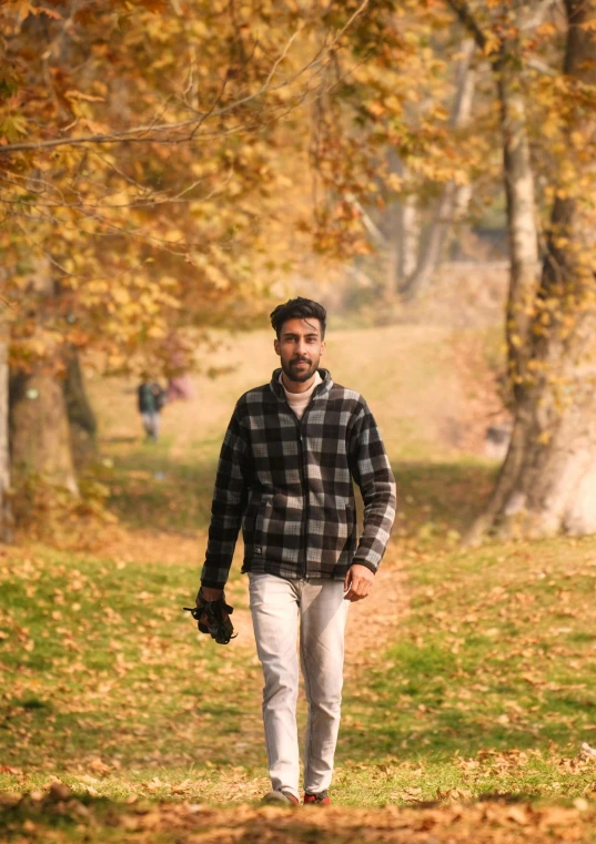 man in a black and white checkered shirt walking through a park