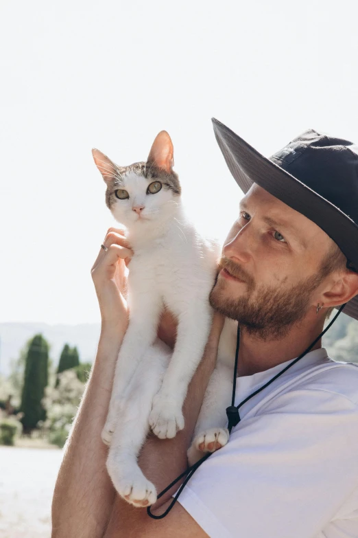 a man is holding a white cat wearing a hat