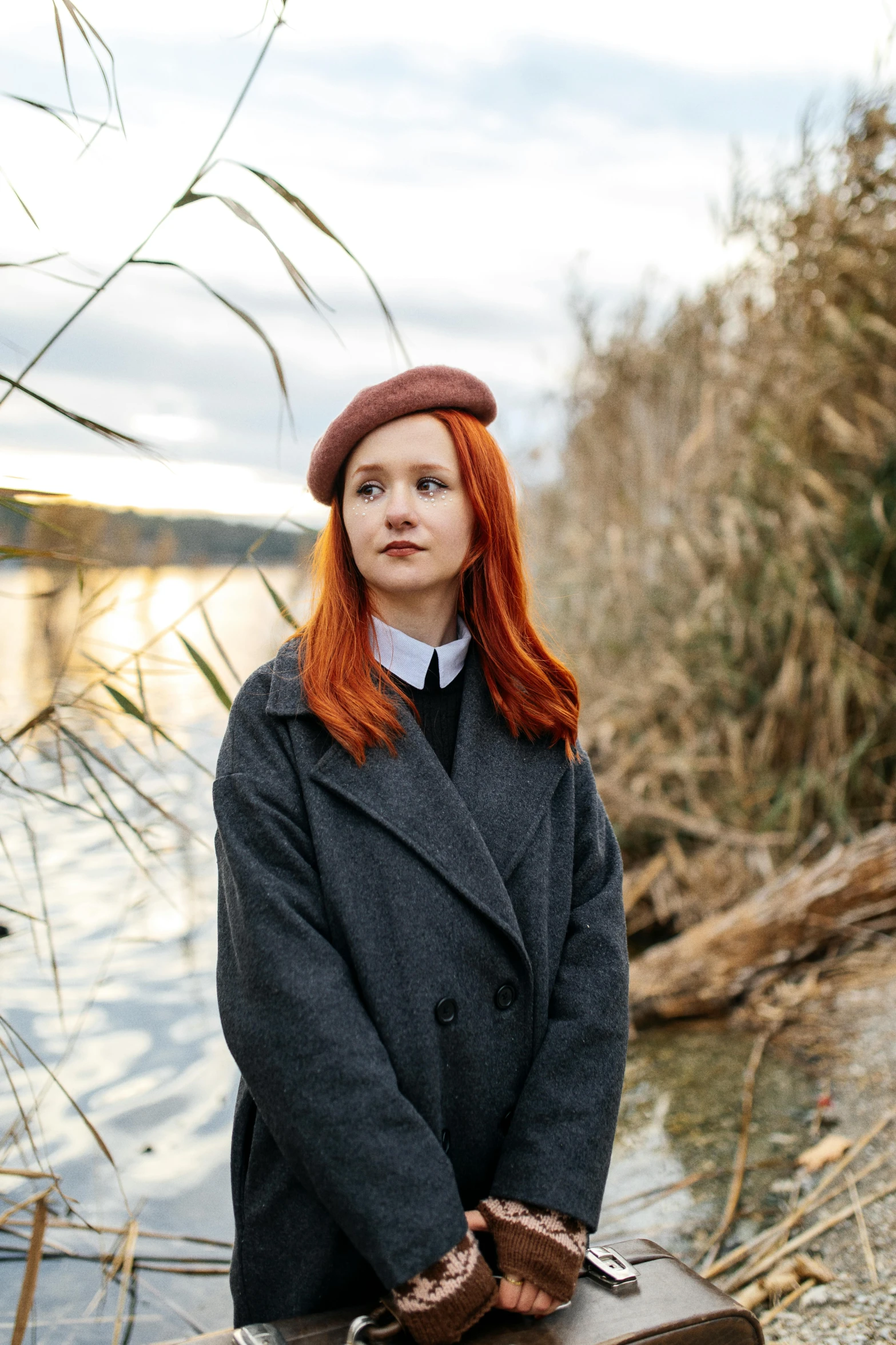 a woman standing near a body of water in a coat and tie