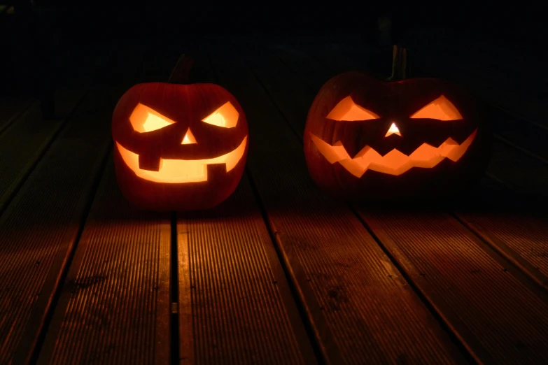 two jack o lanterns sit together on a wooden floor