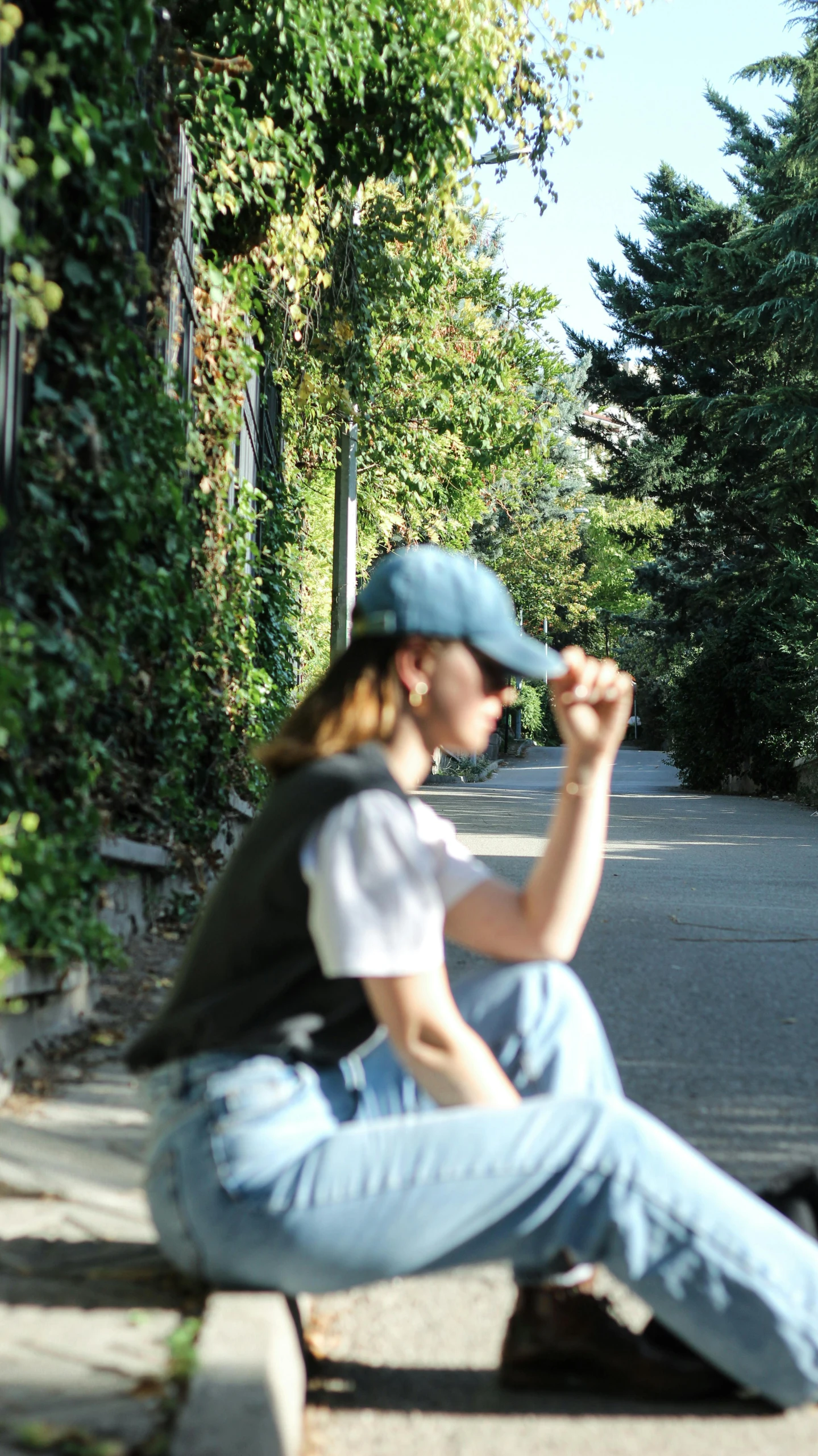 a woman sitting on top of a sidewalk next to a green bush