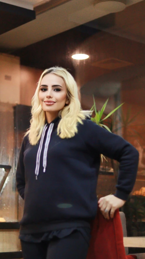 a beautiful young blonde woman standing next to a window