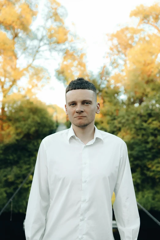 a man with his arms crossed standing in front of a tree