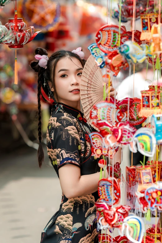 a woman in a traditional chinese dress stands among souvenirs at a market