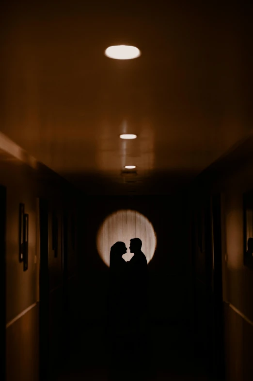 a dark hallway with two people in the doorway, one holding his hand over the other