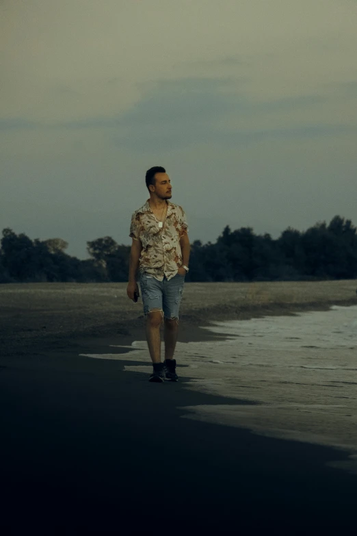 a man walking along the beach with trees behind him