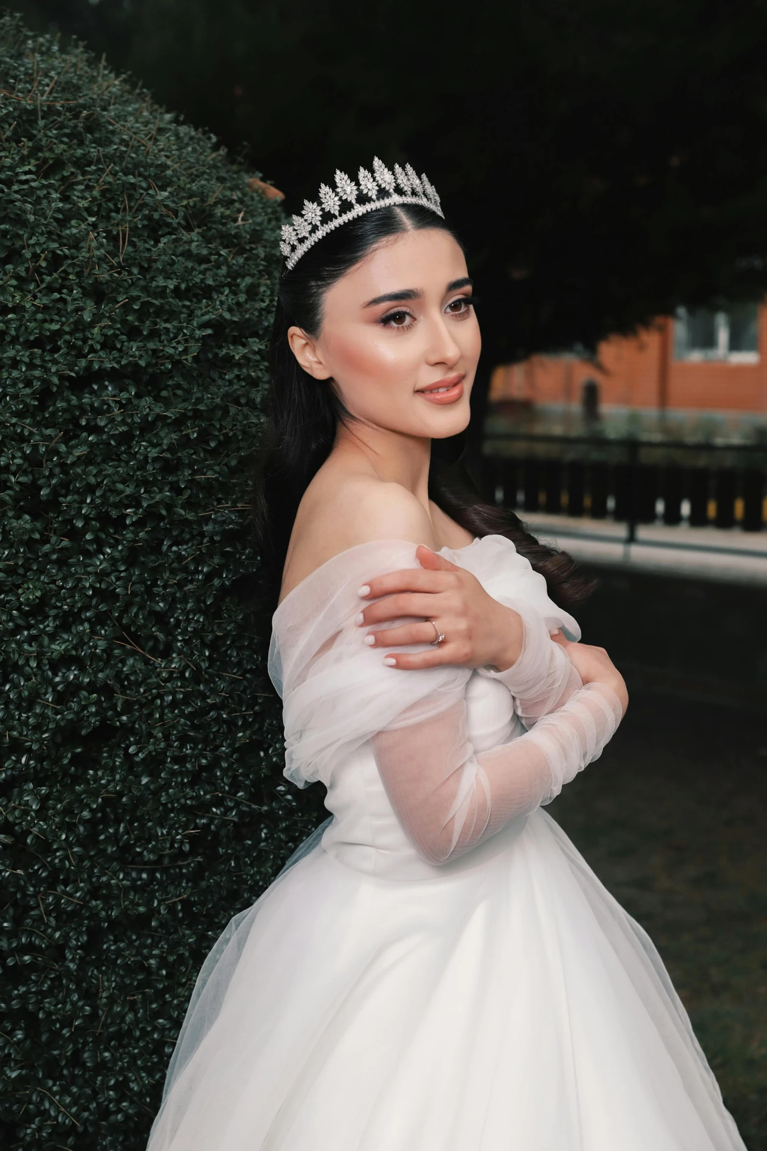 a beautiful woman in a white dress holding her hands against a hedge