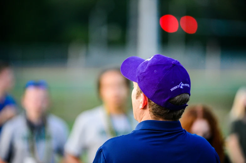 a man wearing a purple baseball hat and staring at a football field