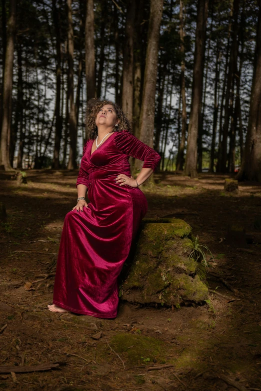 a woman wearing a red dress sitting on a moss covered log