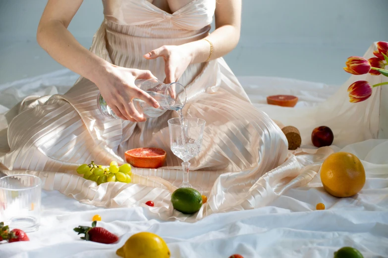 a woman sitting on a bed holding a glass and making a drink