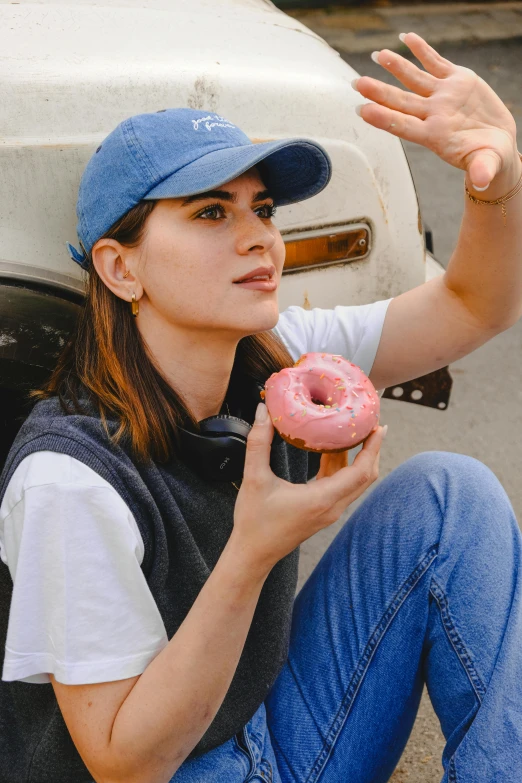 a woman is sitting by the back of a truck eating a pink doughnut