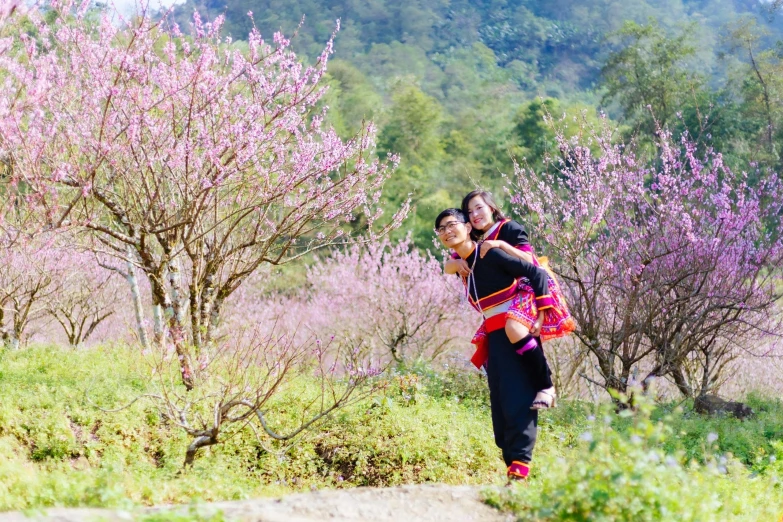 people are walking along a path among trees with pink flowers