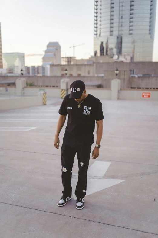 a man in black clothes holding a skateboard on top of a parking lot