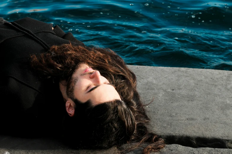 man laying on concrete near water wearing a jacket