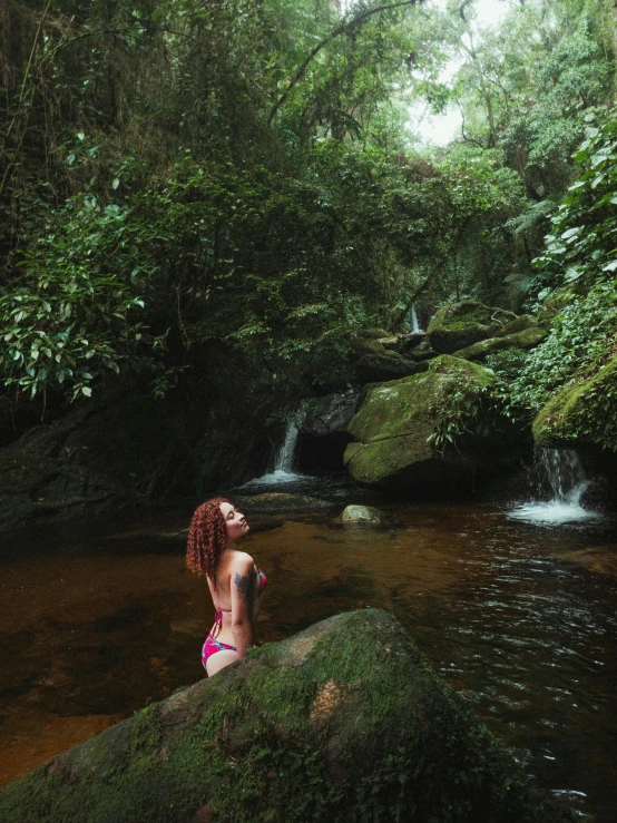 woman with red hair sitting on a rock above stream