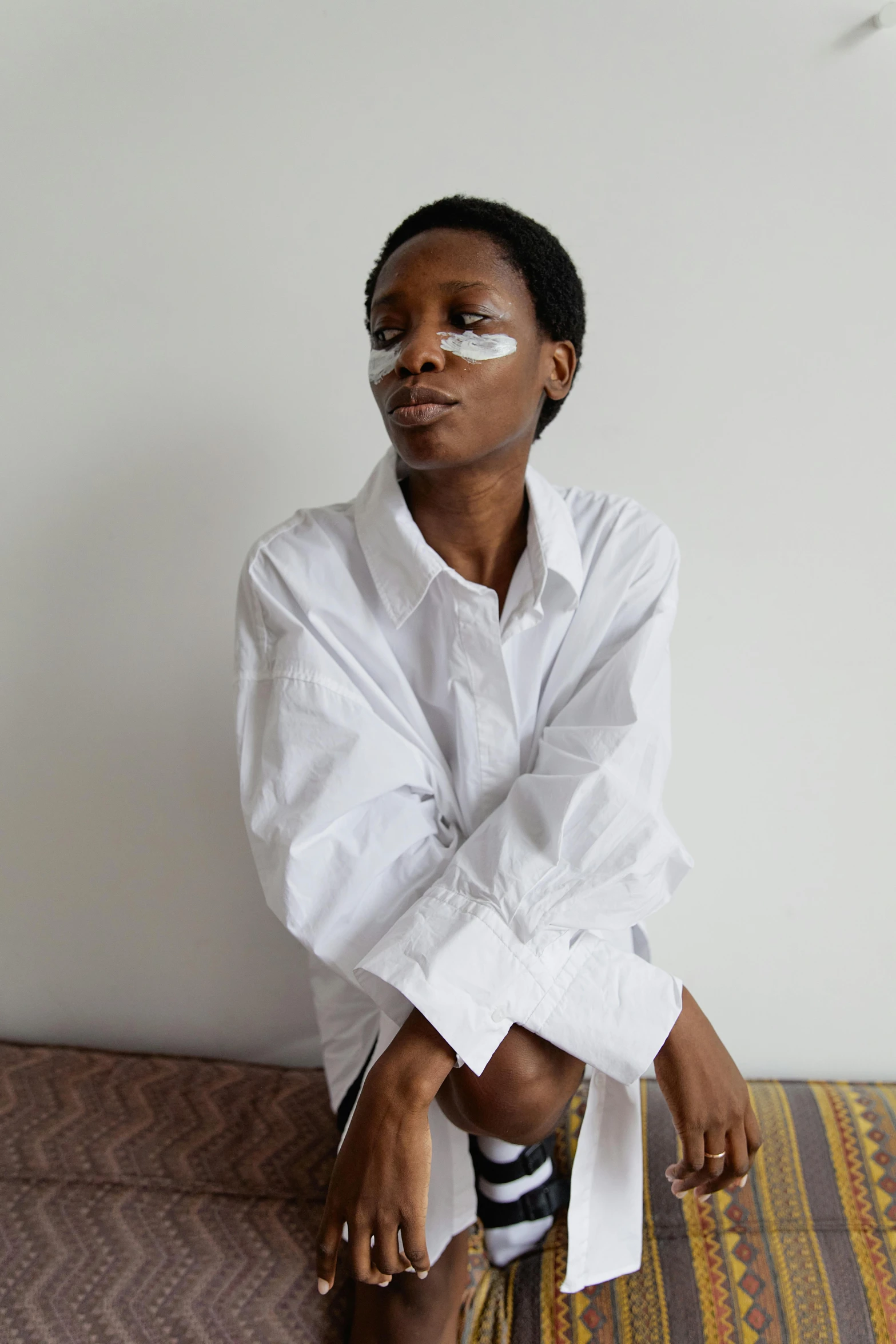 young woman sitting on striped bed sheet in white shirt