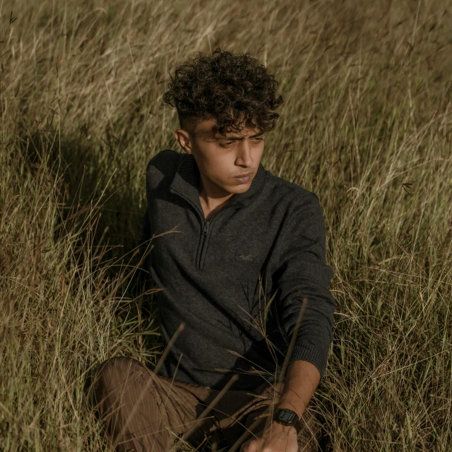 a boy is sitting in tall grass looking