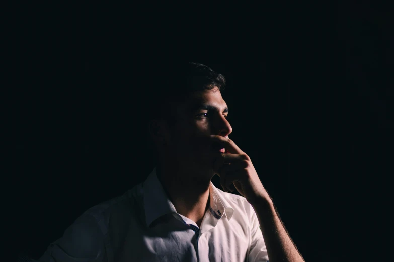 man in dark portrait using left hand to face