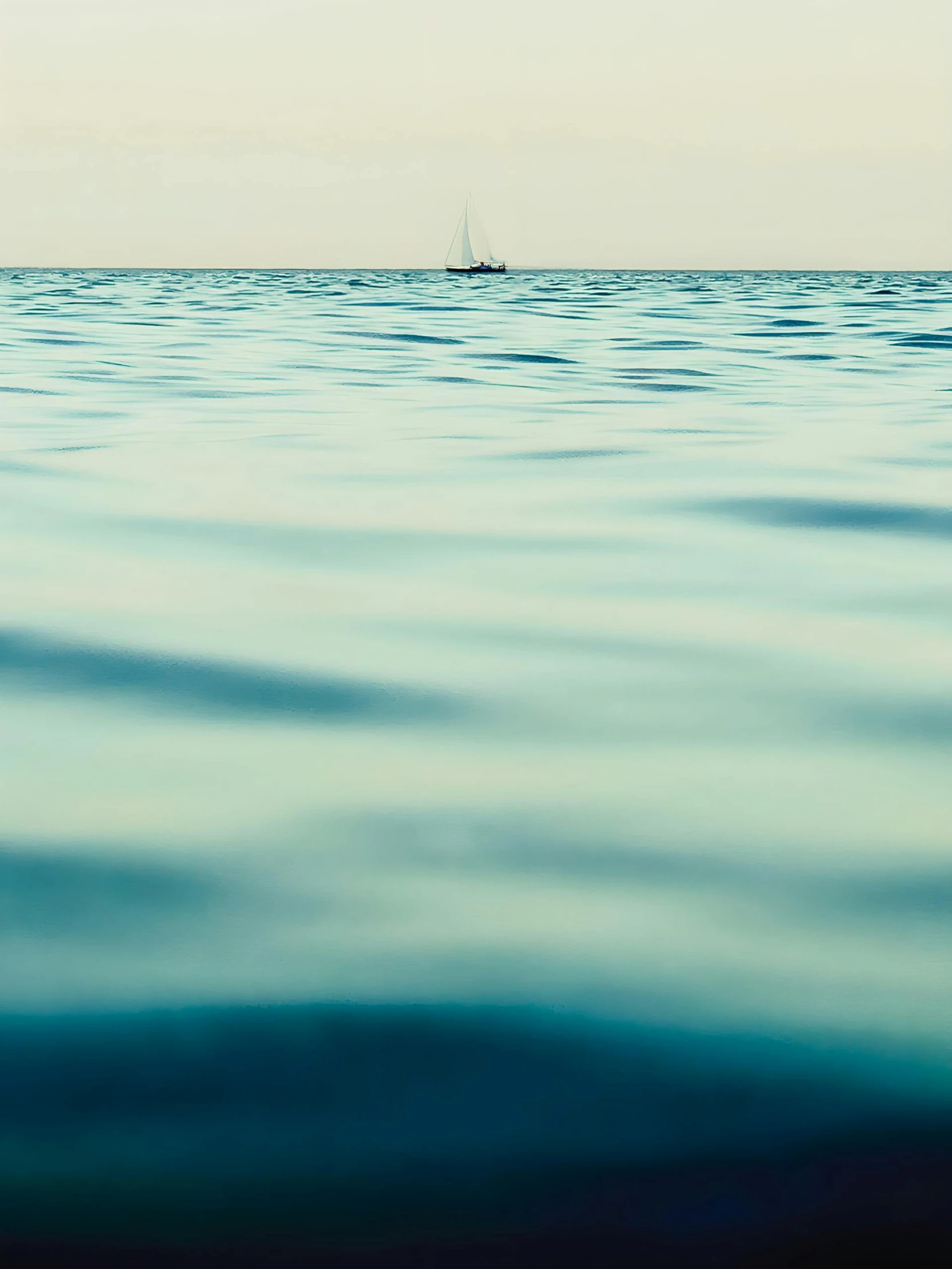 a sailboat is on the horizon of a calm ocean