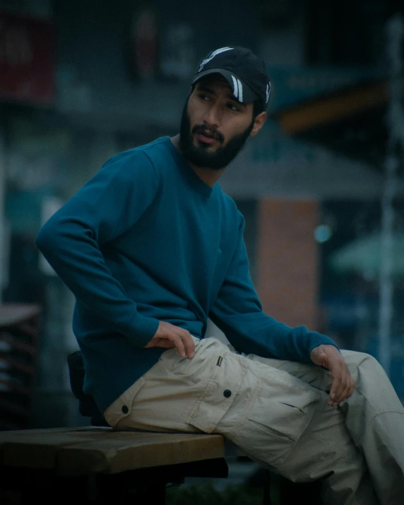 man sitting on bench wearing blue jacket and beige pants