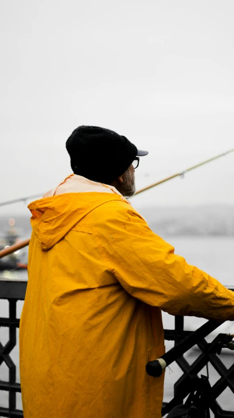 a person in a yellow jacket is fishing from a railing