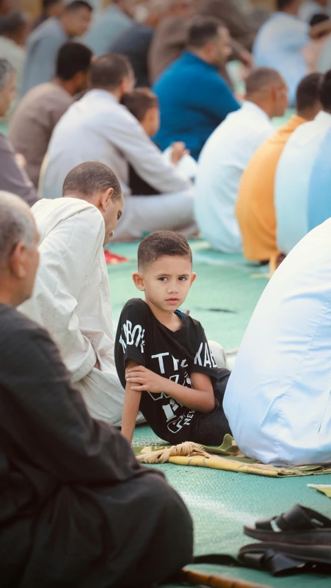 a little boy is sitting on the ground surrounded by people