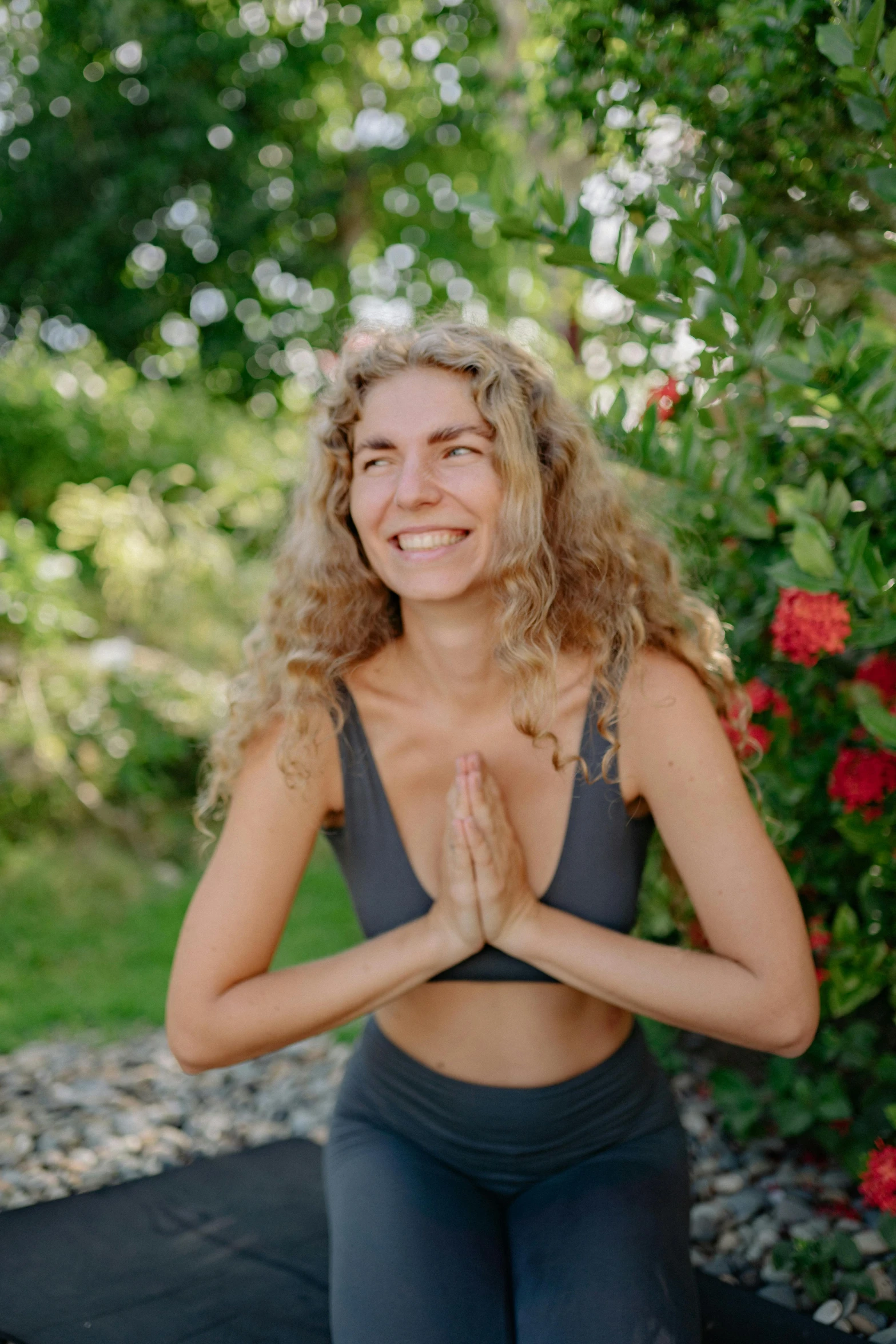 a woman sitting in front of a bush with her hands up