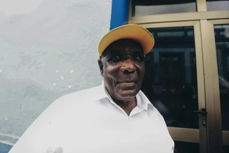 an older man in a yellow hat stands outside the entrance to a building