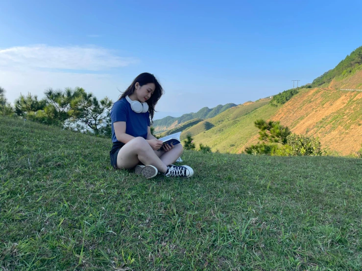 young woman sitting on grassy hillside looking down at valley