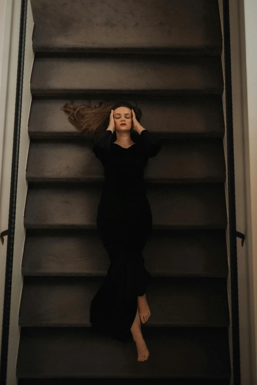a woman in a black dress holding a hair bundle stands on the stairs of a stairwell