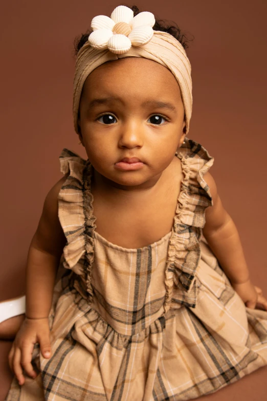 a baby girl wearing a beige dress with a white flower on top