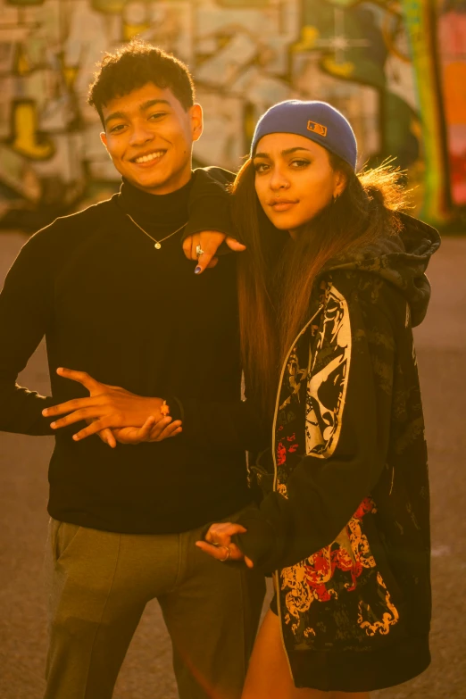 a man and woman posing for a po in front of a wall with graffiti