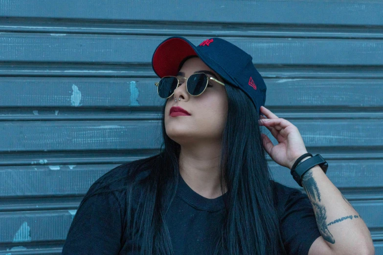 a woman wearing a hat and sunglasses while leaning on the wall