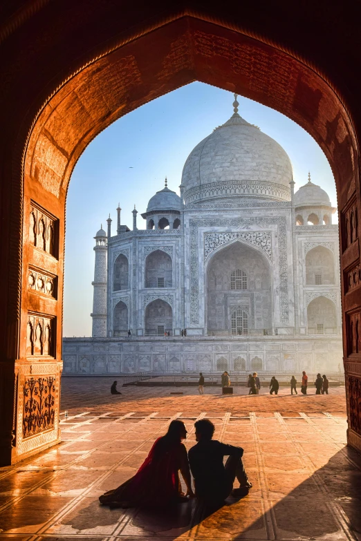 two people sit on the ground in front of a taj