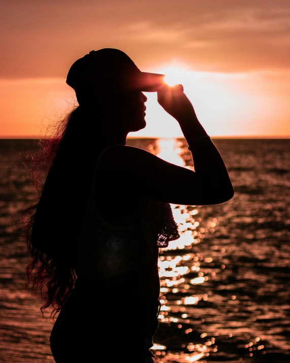 a woman standing by the ocean at sunset