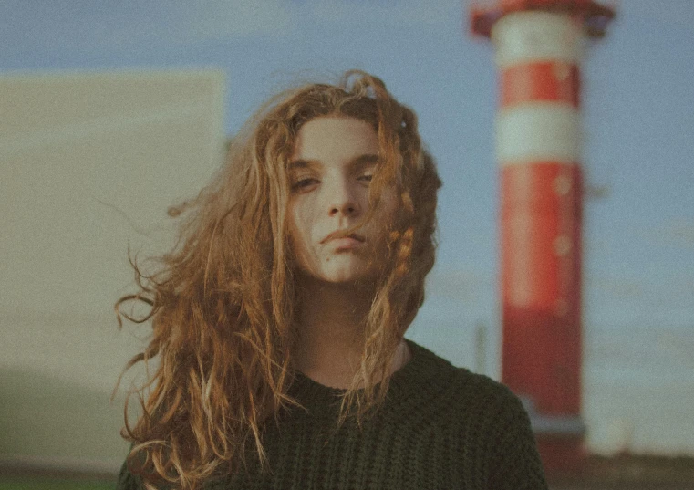 a man with long hair standing next to a light house