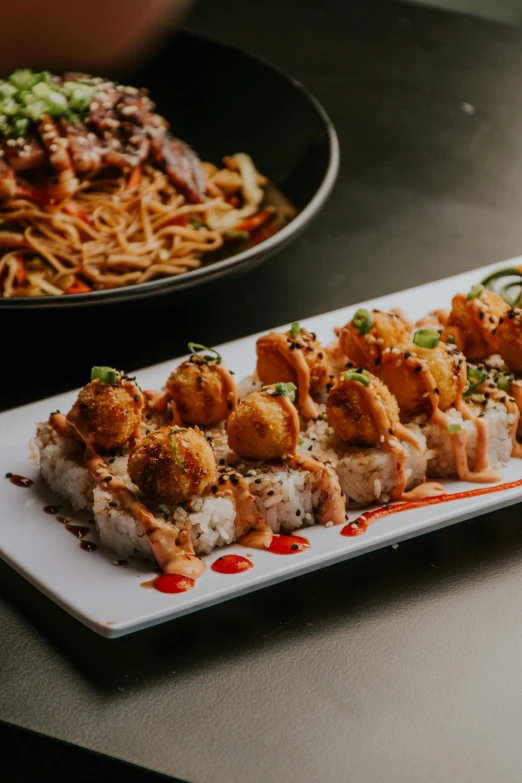 a close up of sushi on a plate with a bowl in the background